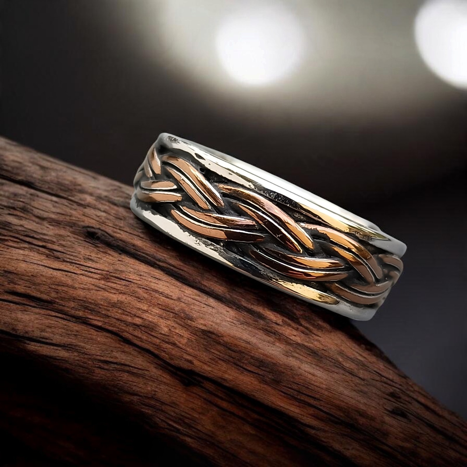 Ring mit drehbarem Flechtband in Bronzeton und silberfarbenen Rändern auf altem Holz