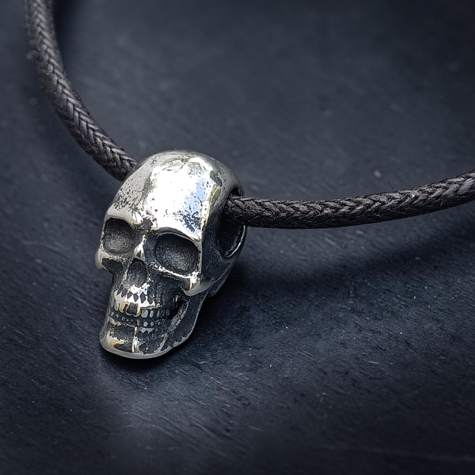 Kleiner Totenkopf-Anhänger aus Edelstahl auf schwarzem Band vor dunklem Schiefer
