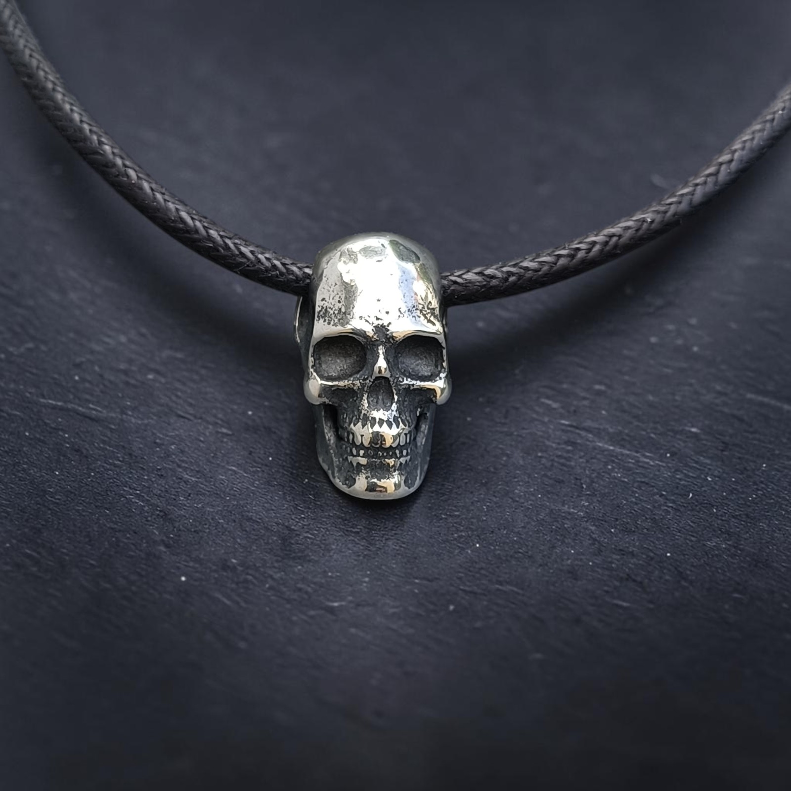 Kleiner Totenkopf am schwarzen Band, frontal auf Schiefer