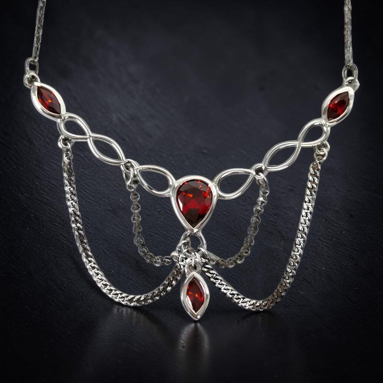 Nahaufnahme eines Gothic Colliers aus 925 Sterling Silber mit roten Zirkonia-Steinen, mehreren Ketten und einem roten Tropfen am Ende, geliefert im Schmuckkarton.
