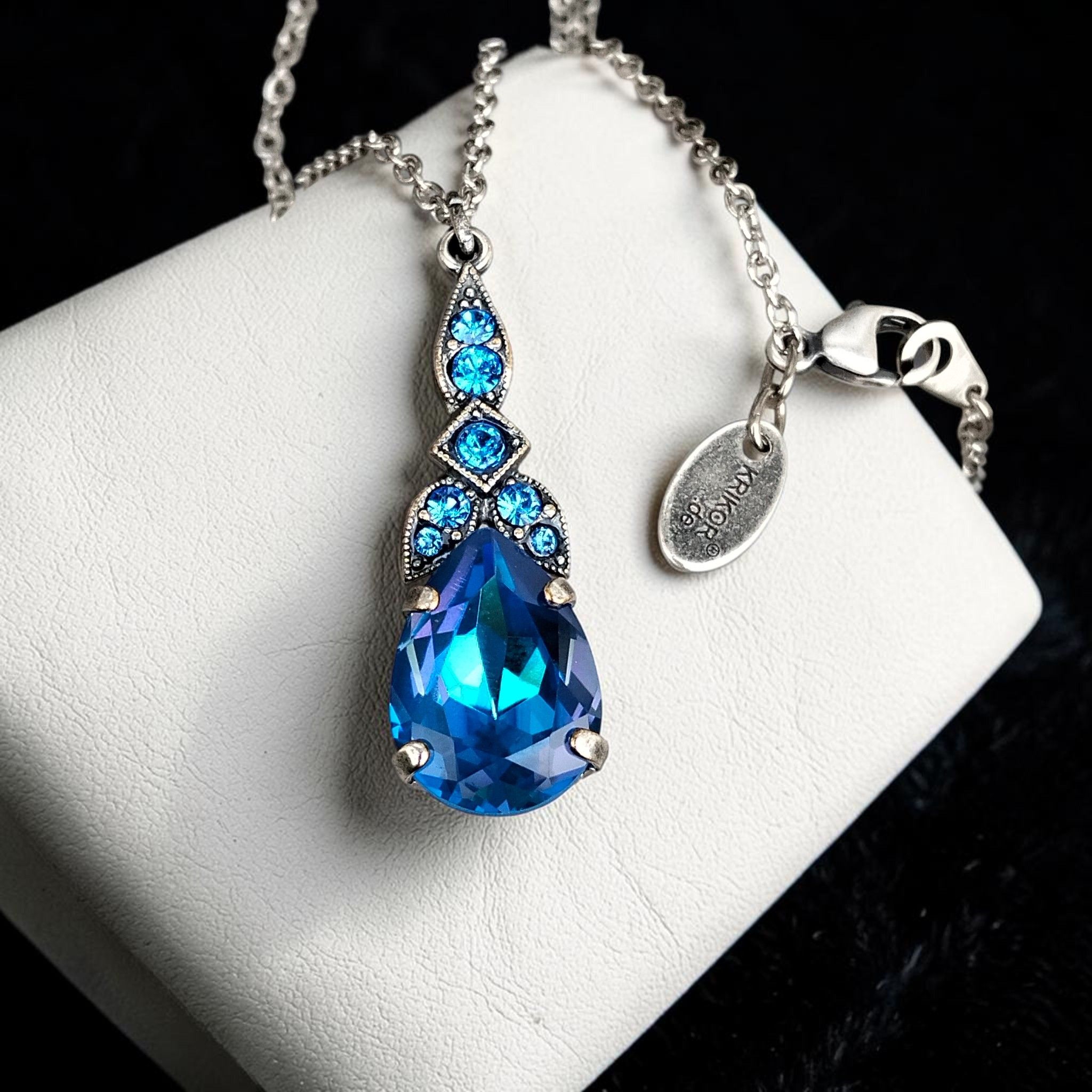 Nahaufnahme des tropfenförmigen blauen Kristallglassteins mit filigraner Art-Déco-Fassung, versilbert
