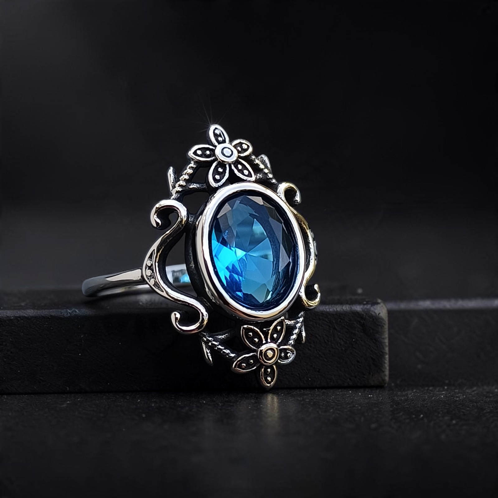 Vintage-Ring aus Edelstahl mit blauem Stein, Blumen und Ranken auf einer dunklen Stufe