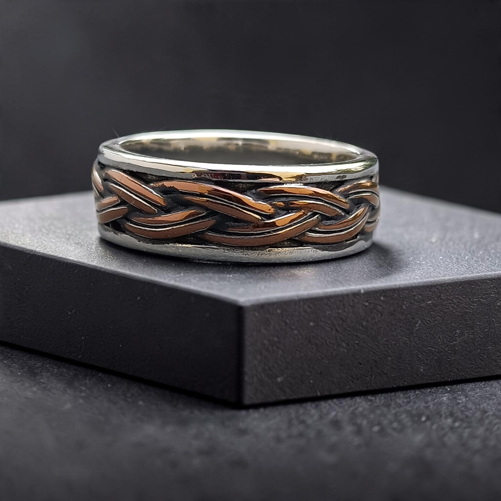 Edelstahlring mit geflochtener Mitte in Bronzeton auf einem schwarzen Sockel