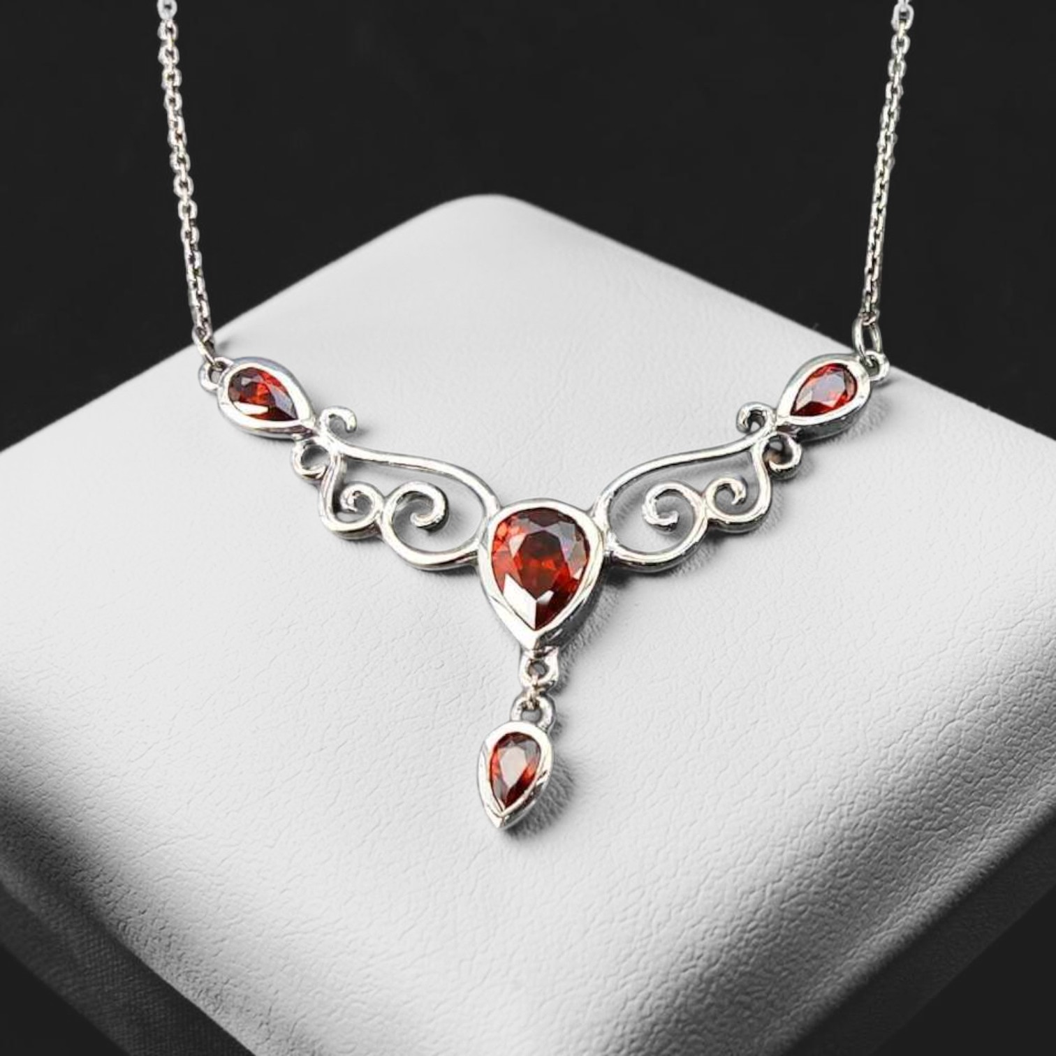 Nahaufnahme eines verspielten Colliers aus 925 Sterling Silber mit roten Zirkonia-Steinen und einem roten Tropfen am Ende, geliefert im Schmuckkarton.