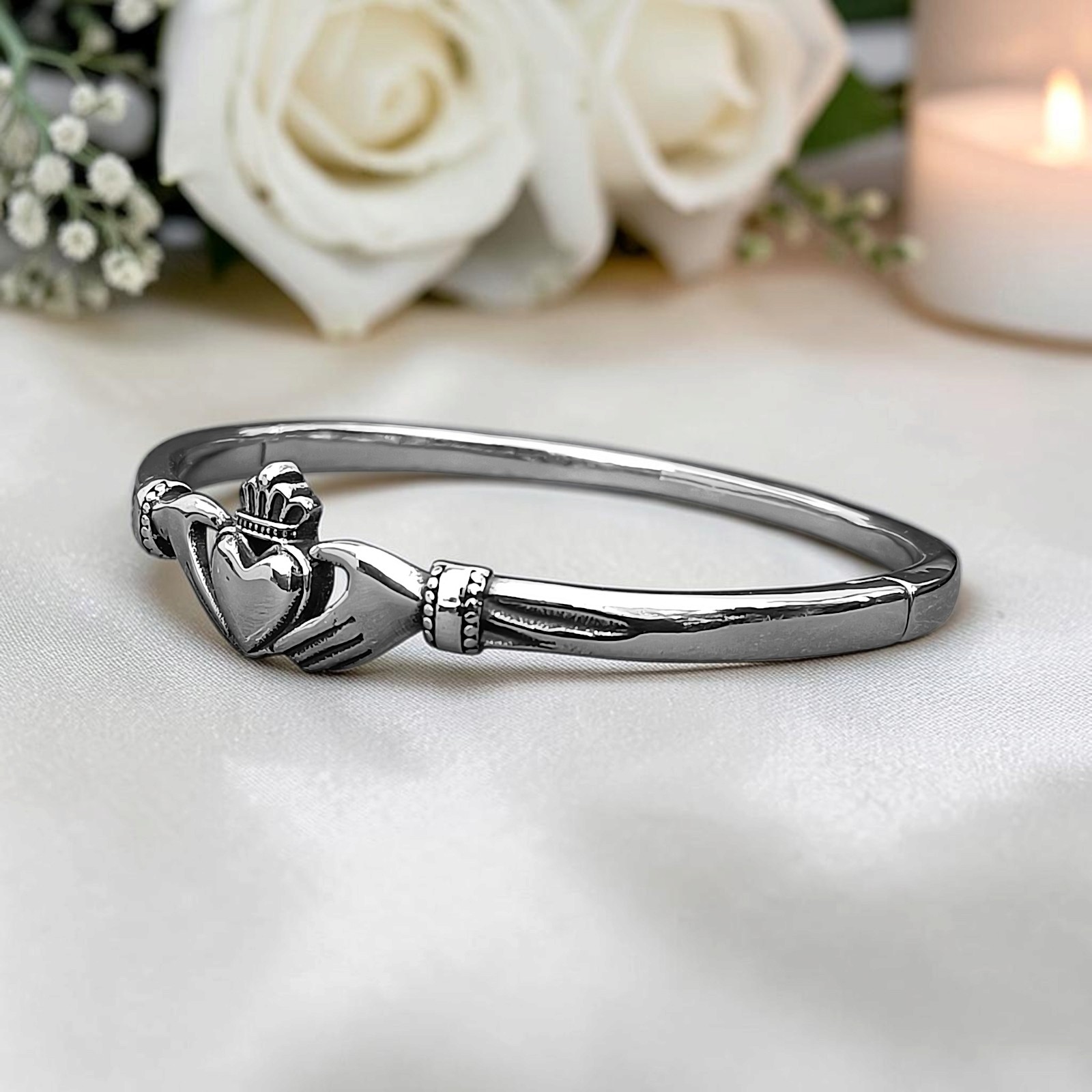 Claddagh-Armreif vor weißen Rosen und Kerze