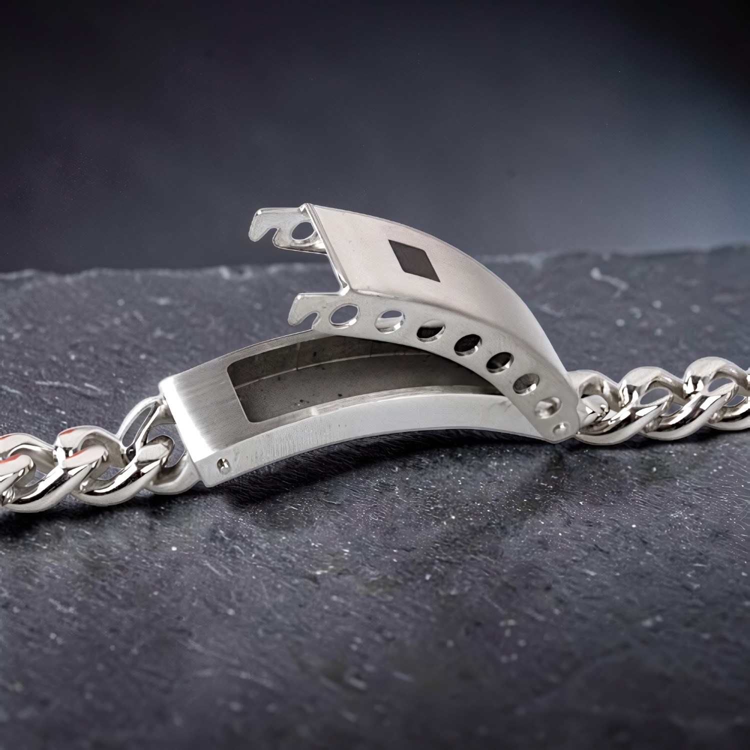 Panzerarmband aus mattiertem Edelstahl mit aufgeklappter Platte auf dunklem Grund