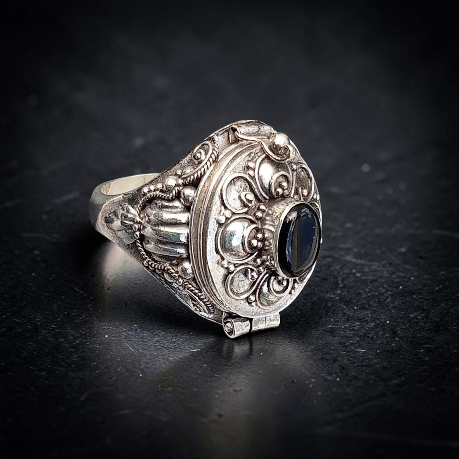 Giftring mit ovalem Onyx in Spiralblüte, schräg auf dunklem Schiefer