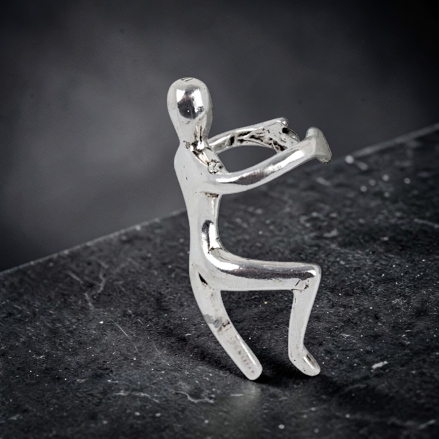 Silberne Ohrklemme als kletternde Figur, die sich mit beiden Armen über eine Kante zieht