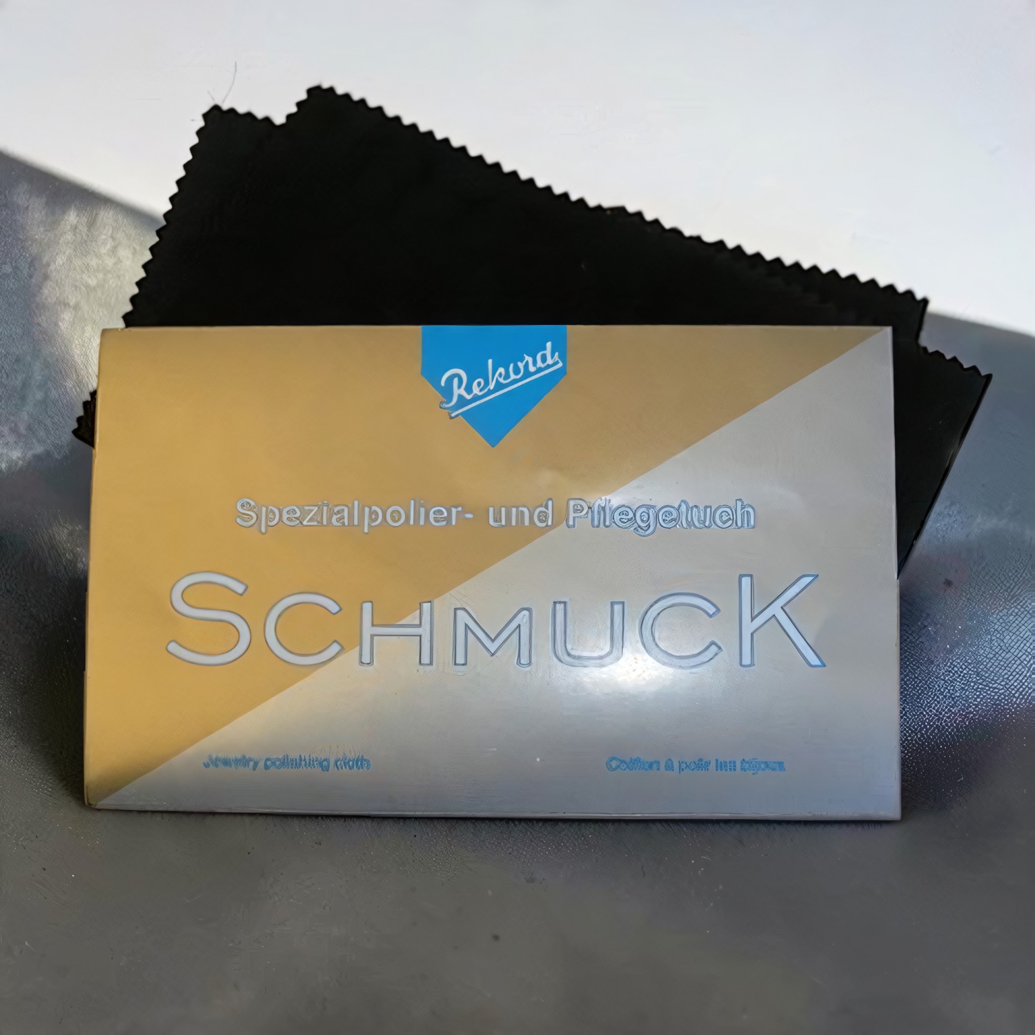 Schwarzes Schmuckpoliertuch hinter dem Briefchen mit der Aufschrift Spezialpolier- und Pflegetuch Schmuck