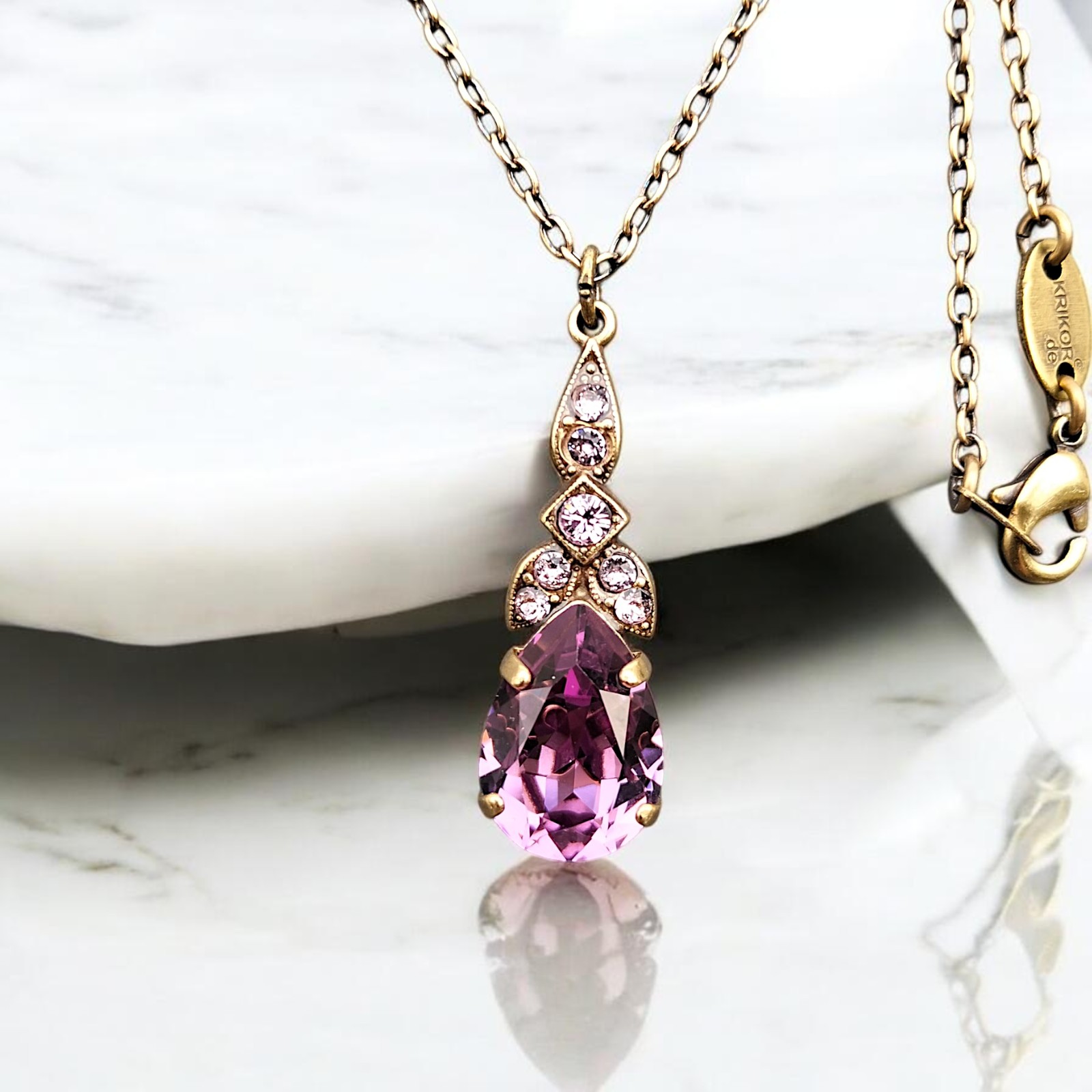 Tropfen in Rosa-Violett unter goldfarbenem Ornament mit klaren Steinen