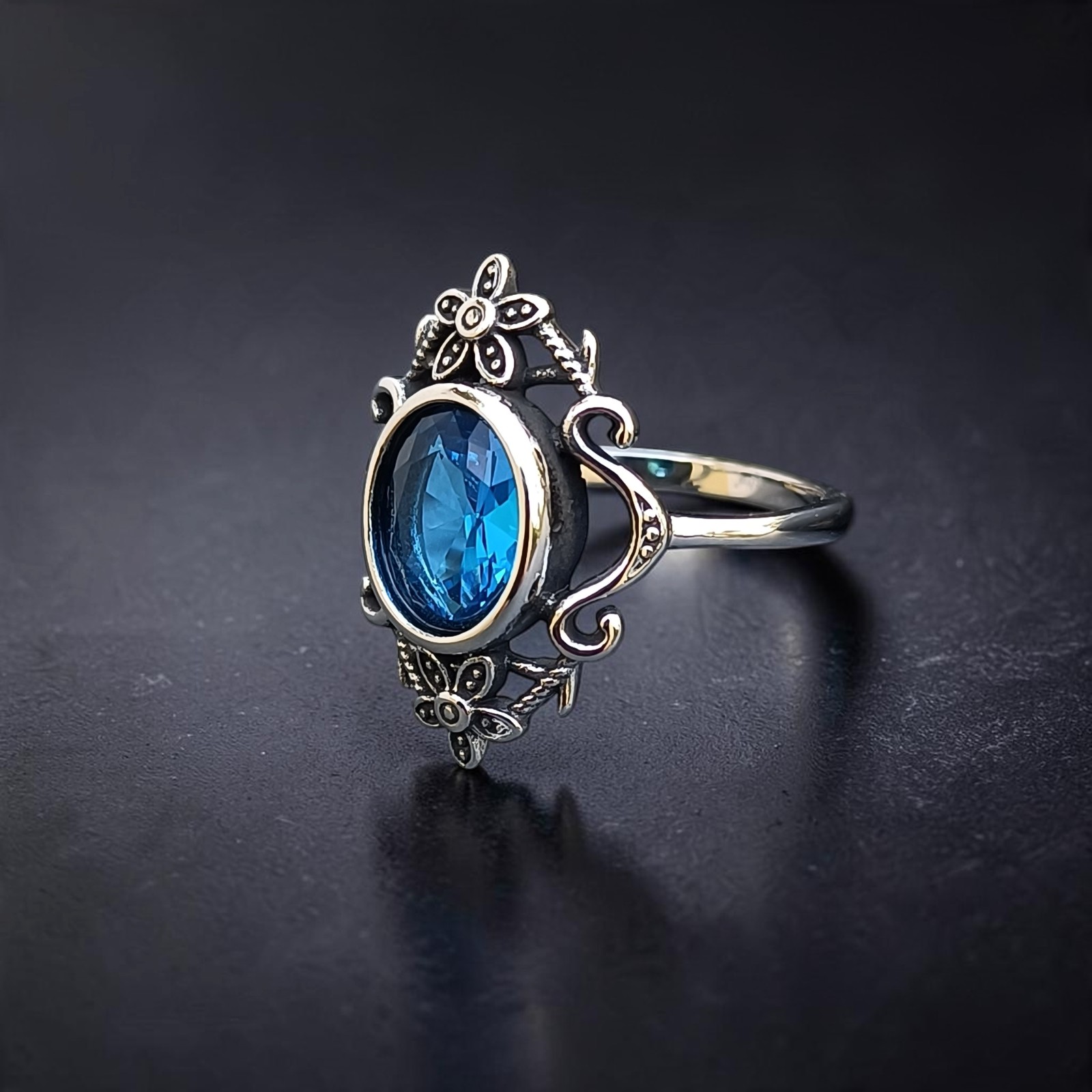 Ring mit ovalem blauem Zirkonia und Rankenornament schräg von der Seite